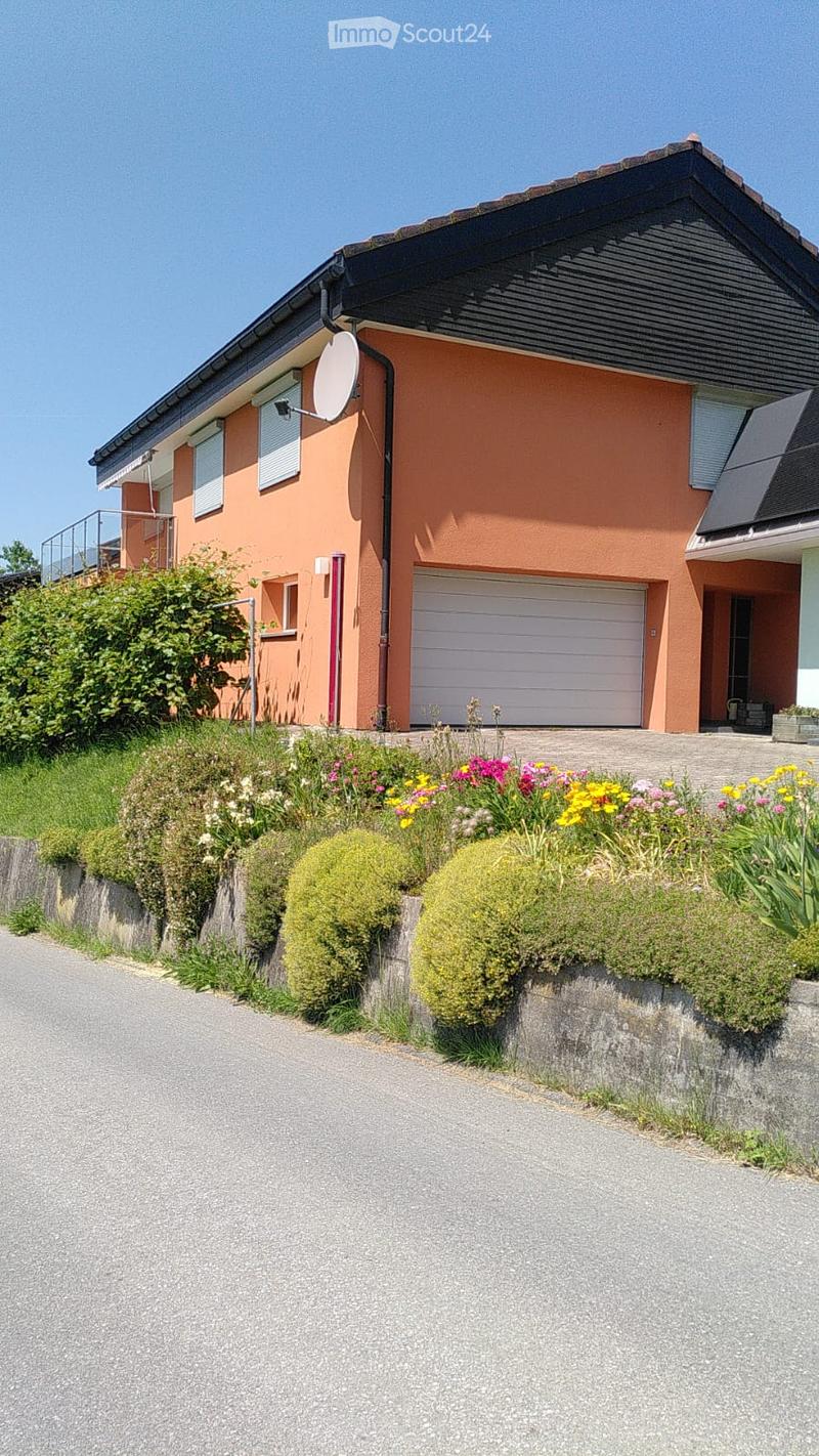Two-story house with orange exterior, white garage door, satellite dish, and well-maintained garden with colorful flowers and shrubs.