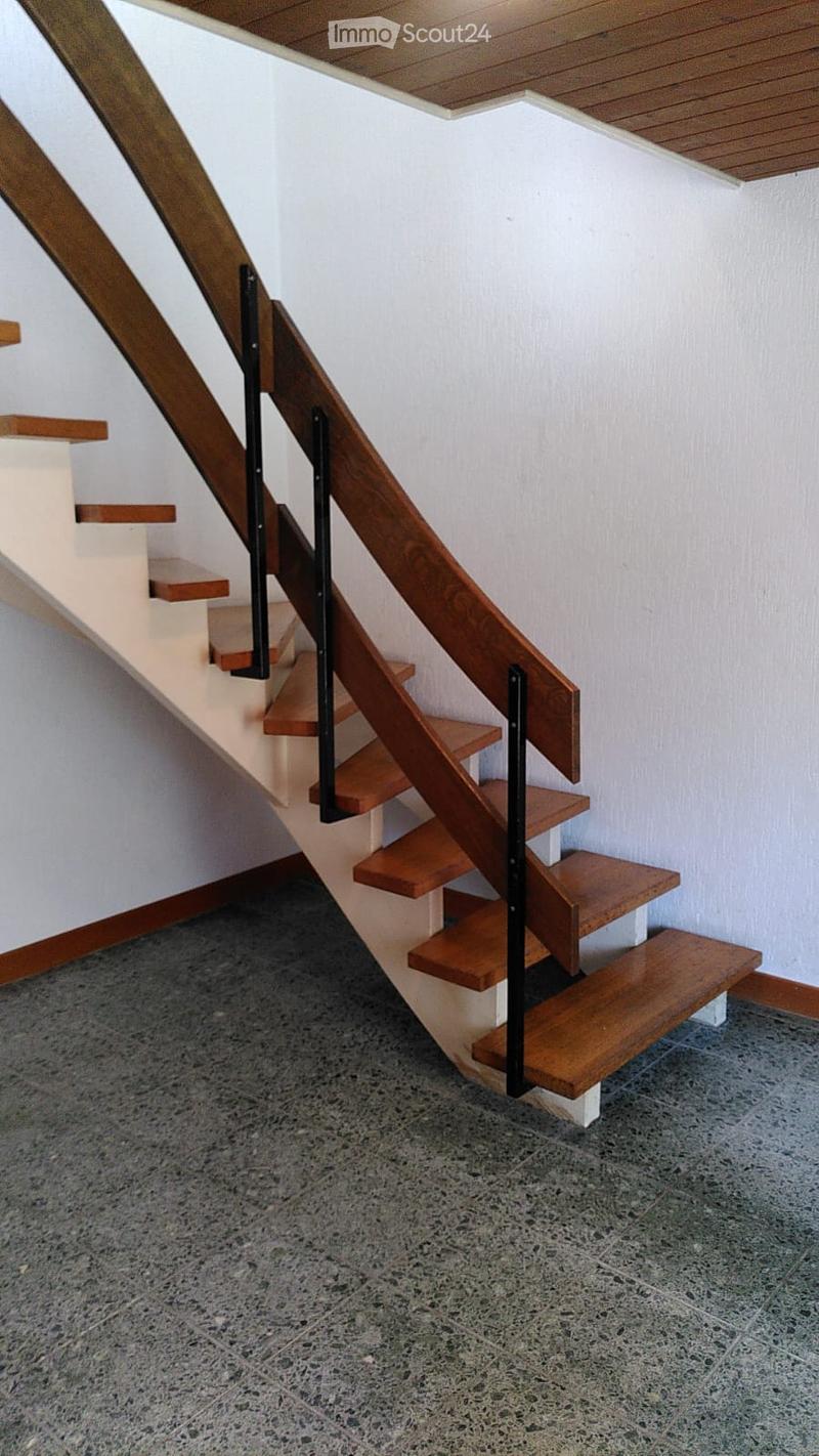Wooden staircase with metal railing, white walls, and a grey concrete floor.