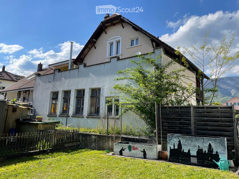 2 story house, white exterior, brown roof, multiple windows, fenced yard, small garden, mural