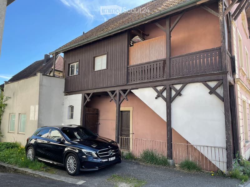 2 story house, brown wooden exterior, balcony, black car parked in front