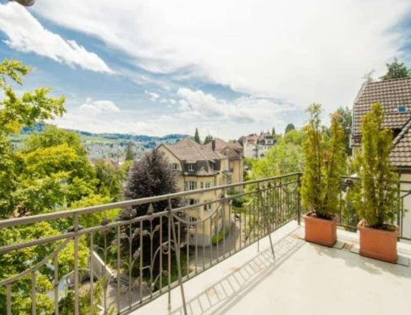 Balcony with metal railing, two potted plants, view of the city