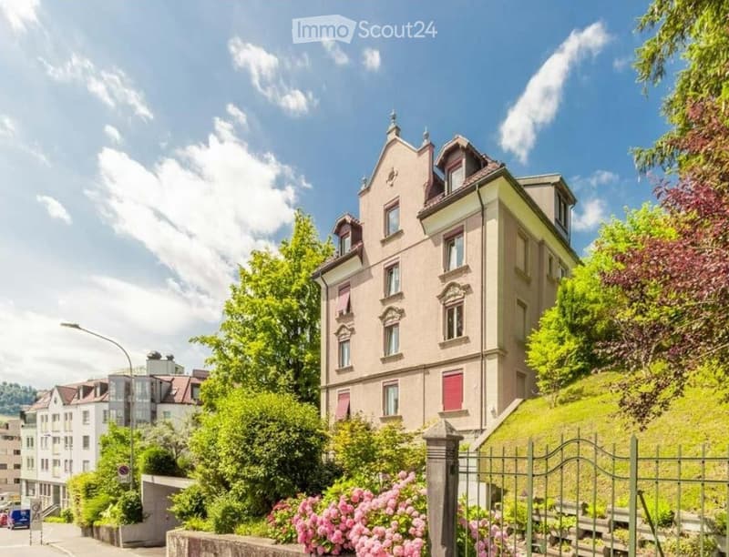 3 story building, pink exterior, red shutters, surrounded by greenery, street light, gate