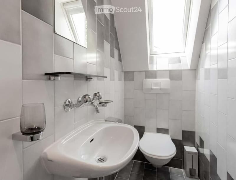 white tiled walls, white sink, silver faucet, white toilet, mirror, glass holder, skylight