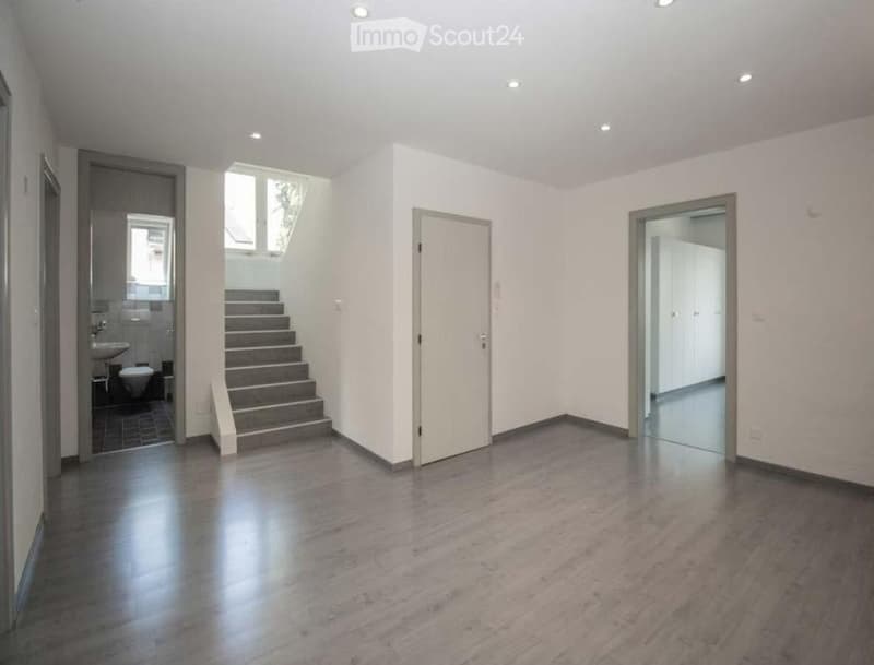 Empty room with wooden floor, white walls, staircase, and doors leading to other rooms
