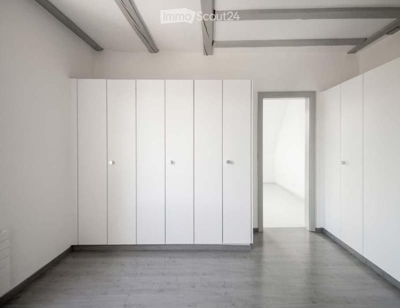 Empty room with white walls, wooden floor, built-in wardrobes, and an open door.