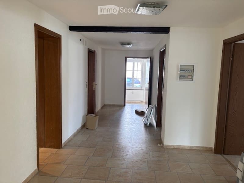 Empty hallway with tiled floor, wooden doors, and a window leading to another room.