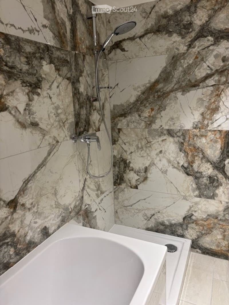 Bathroom with marble walls, bathtub, shower, and shower head
