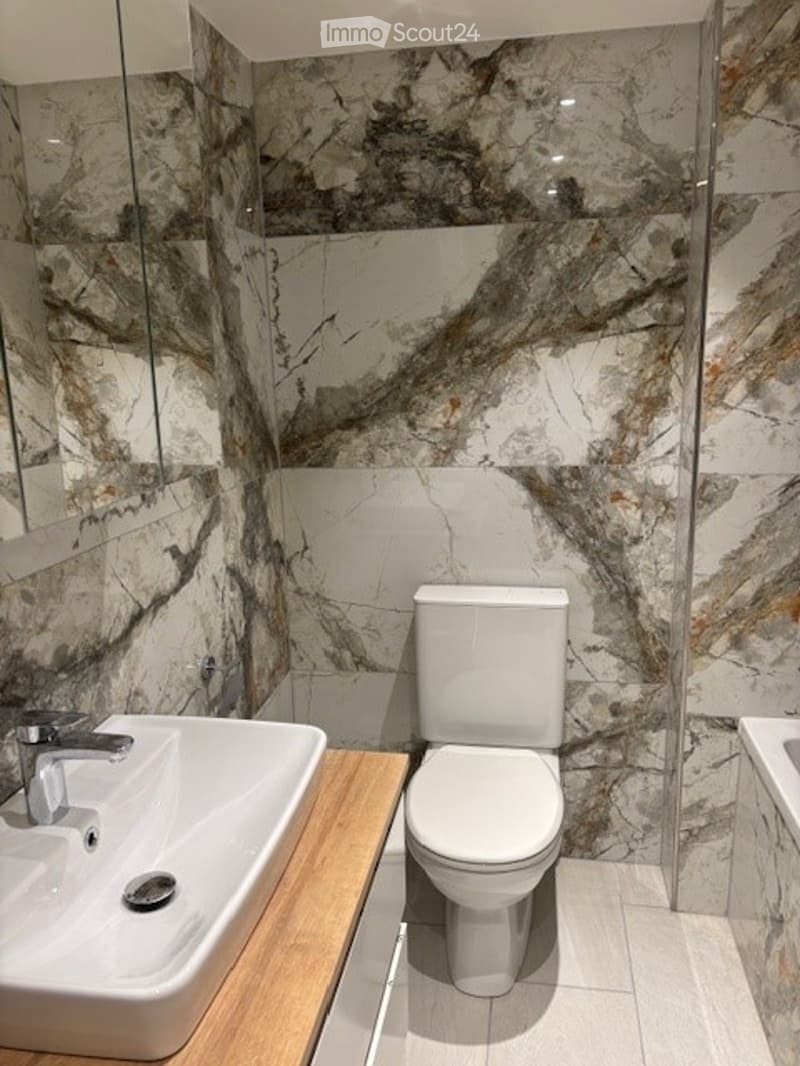 Bathroom with marble walls, white sink, white toilet, wooden countertop, mirror