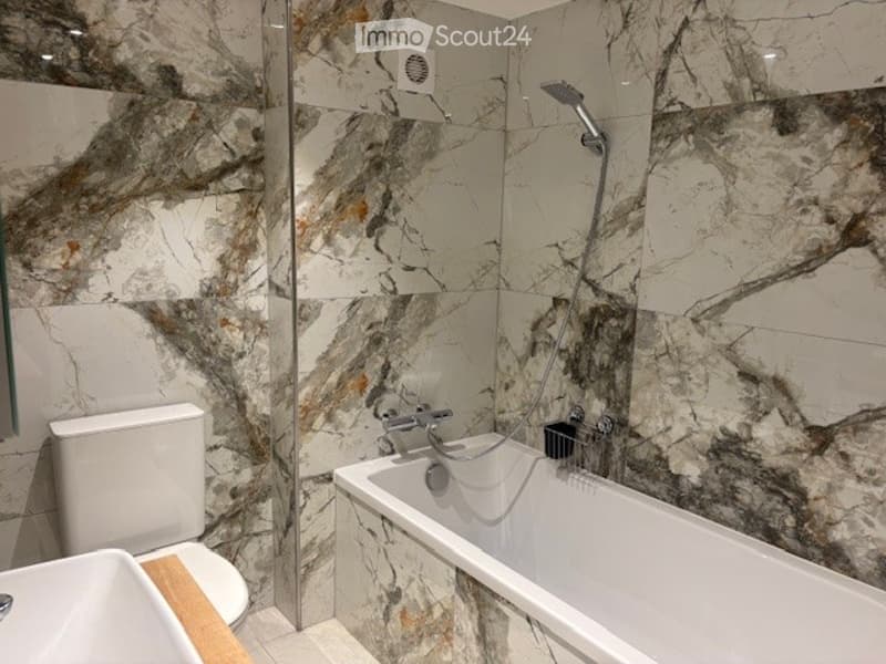 Bathroom with marble tiles, bathtub, shower, toilet, sink, and a glass partition.