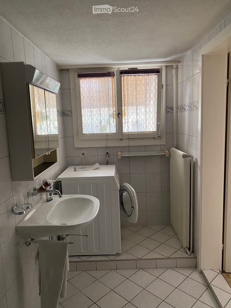 white tiled walls, white sink, white washing machine, white shower, white radiator, mirror, glass cup, towel