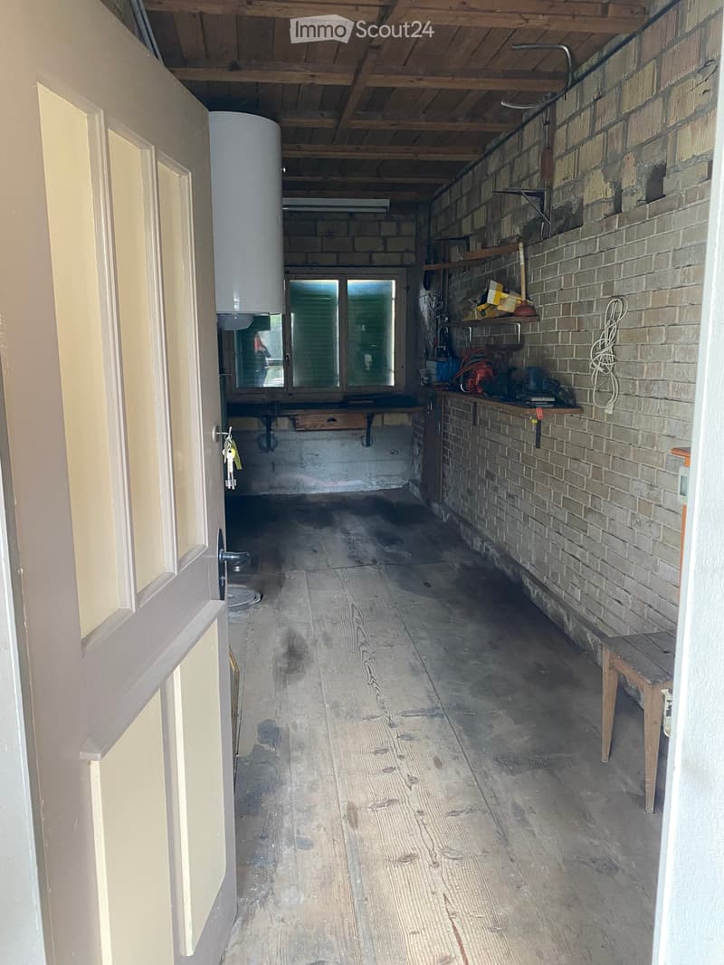 Empty room with wooden floor, brick wall, shelves, and a window.