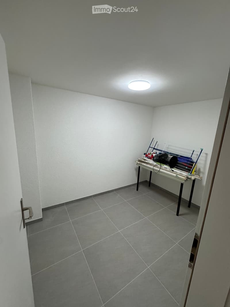 Empty room with white walls, gray tiled floor, ceiling light, table with items
