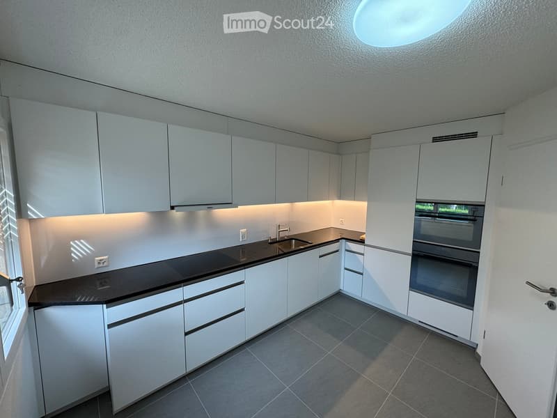 modern kitchen with white cabinets, black countertops, integrated appliances, and a circular ceiling light