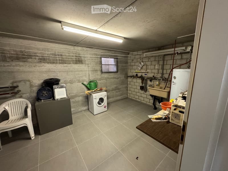 A small room with a washing machine, a chair, a table, and a sink.