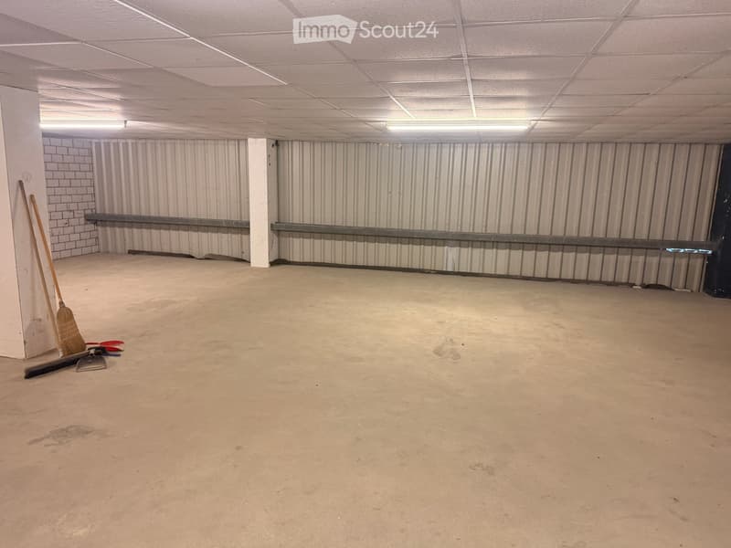 Empty room with concrete floor, white walls, metal beams, and ceiling lights