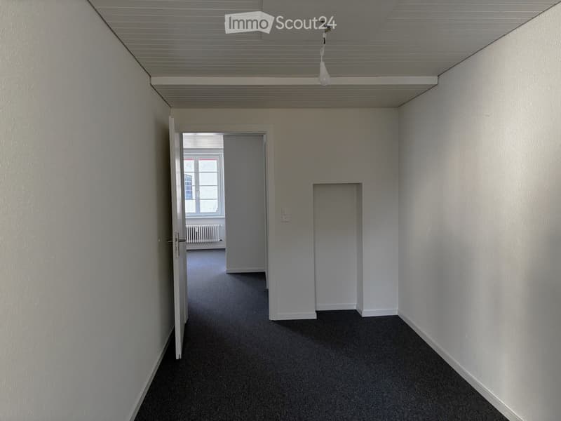 Empty room with white walls, black carpet, open door, window, radiator, ceiling lamp
