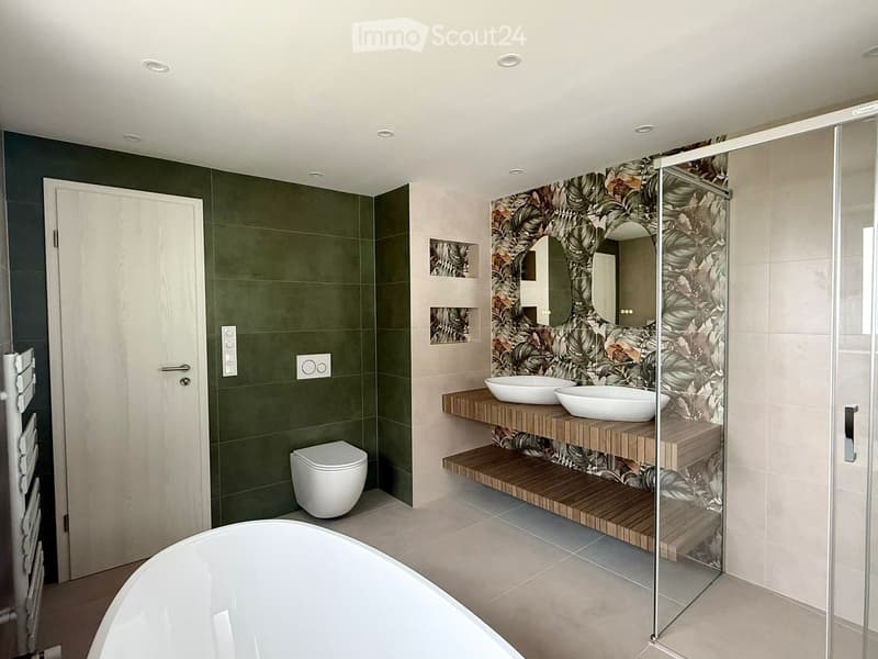 modern bathroom with green tiles, white bathtub, two sinks, glass shower enclosure, white toilet, wooden shelves