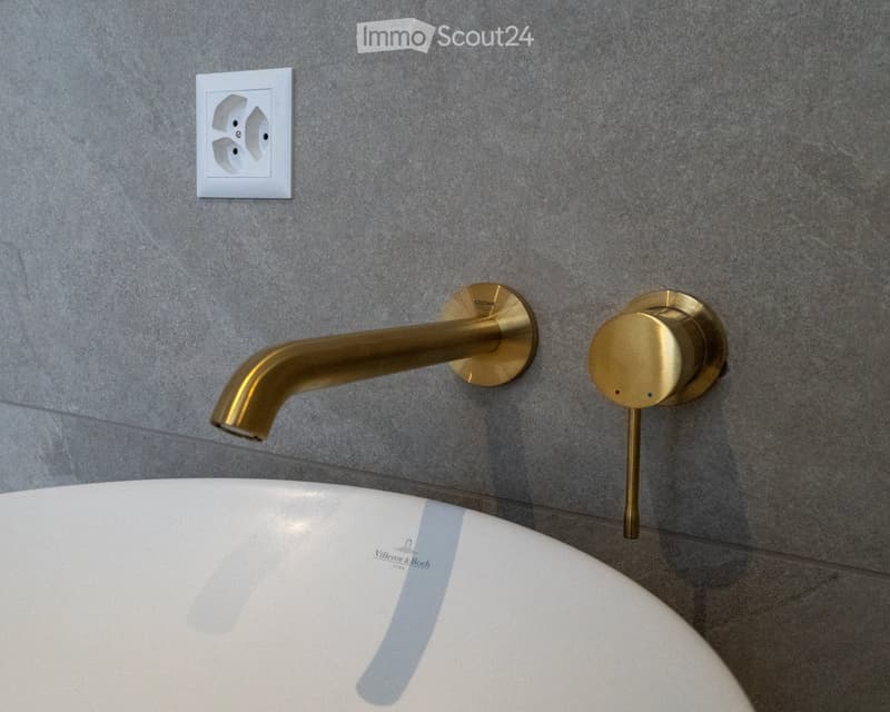Bathroom sink, gold faucet, power outlet, grey wall