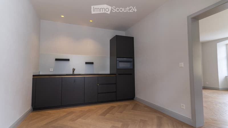 modern kitchen with black cabinets, wooden floor, white walls, built-in oven, sink, faucet, power outlets