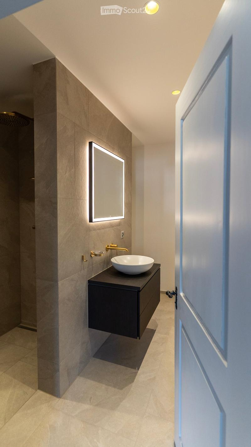 Bathroom with a white sink, a mirror with a light, a shower, and a black cabinet