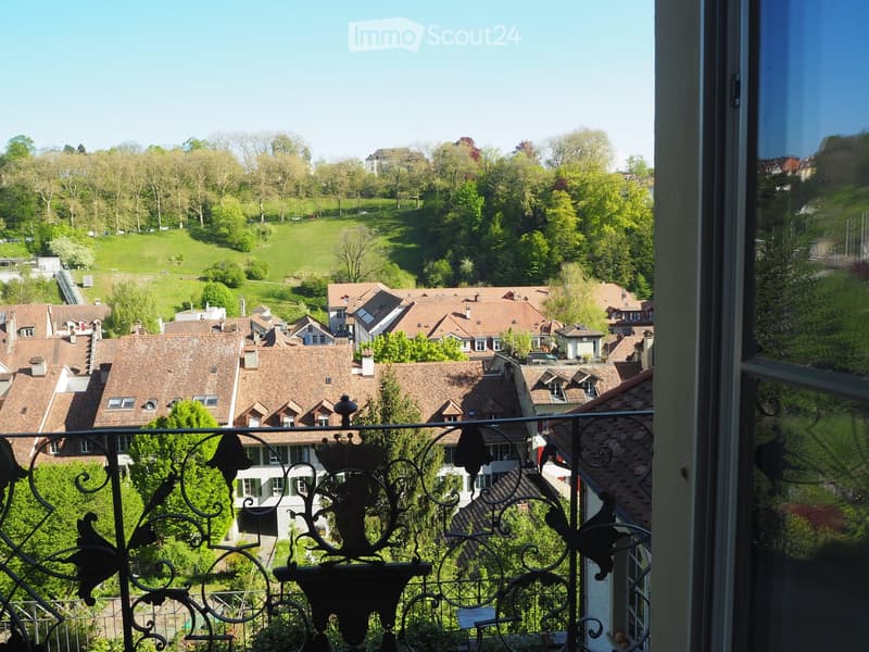 View from balcony of a town with many houses, green hills, and trees