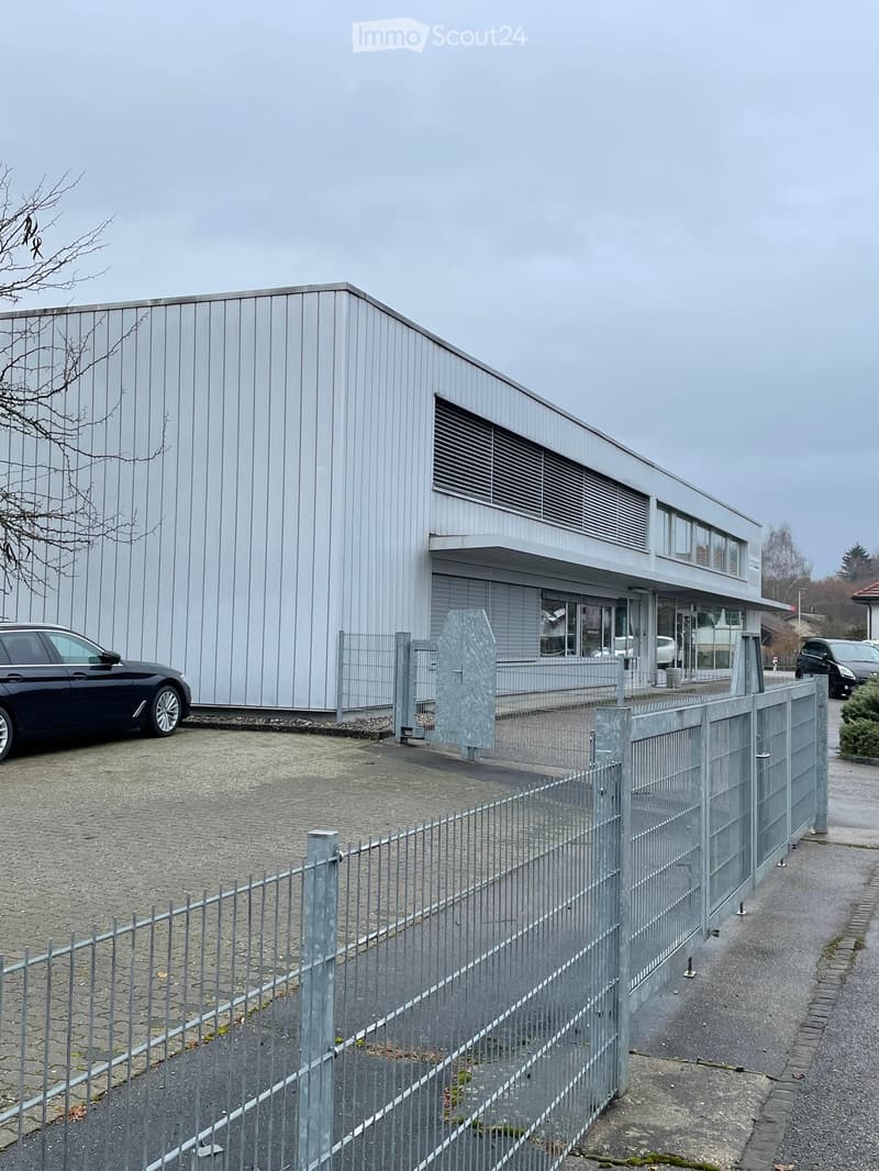 a single story industrial building with several windows and a grey car parked in front