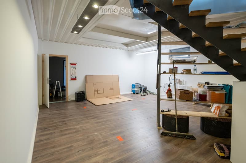 Empty room with wooden floor, white walls, open door, storage boxes, ladder, shelves, and various items