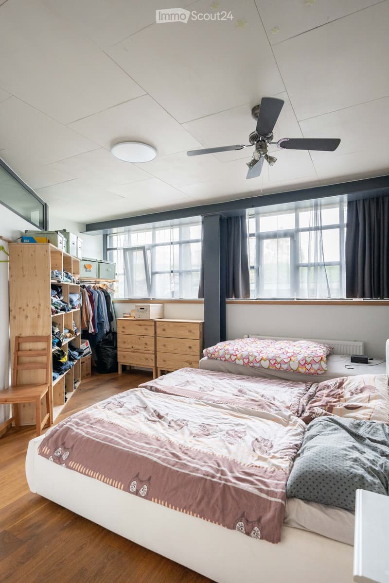 Bedroom with two beds, wooden wardrobe, ceiling fan, wooden floor, large windows, wooden chair, radiator