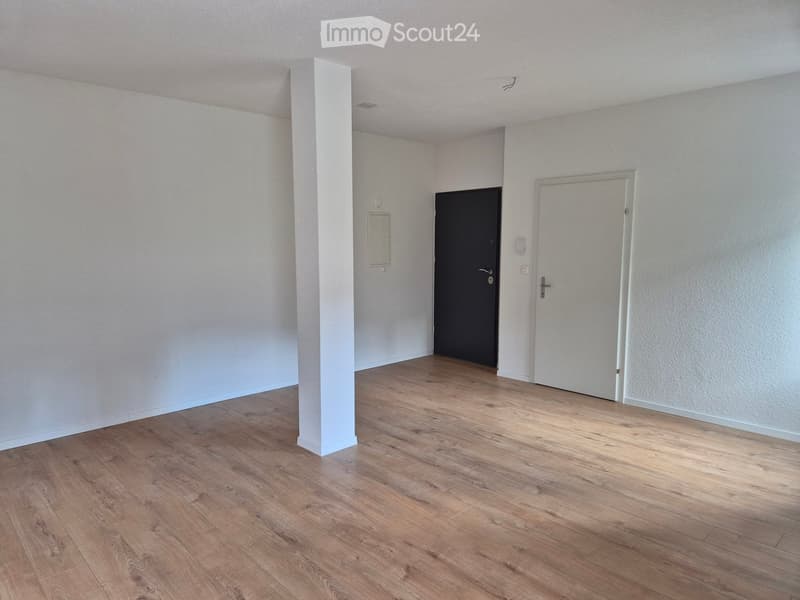 Empty room with light-colored walls and wooden flooring, featuring a central column and two doors.