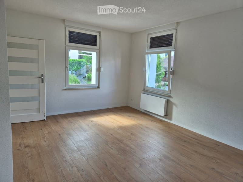 Empty room with wooden flooring, white walls, two windows, and a radiator under one window.