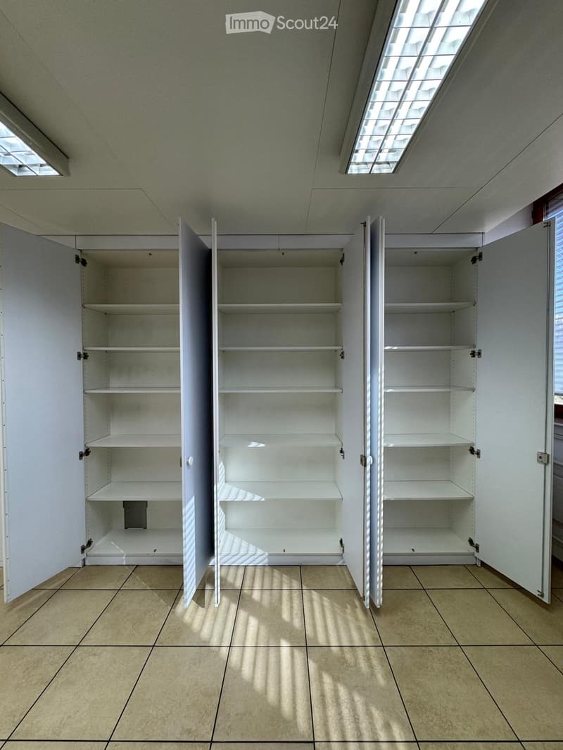 Empty room with three large white cabinets, tiled floor, and ceiling lights