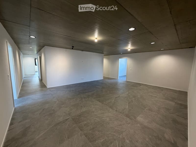 Empty room, white walls, gray tile flooring, recessed ceiling lights, two doors on the left side, one door on the right side