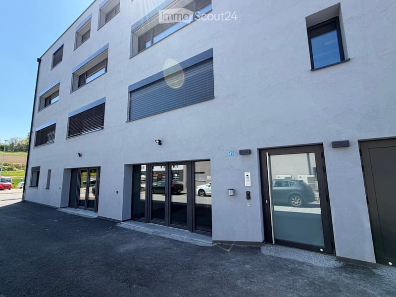 Modern apartment building with glass doors, windows, and a parking area in front.