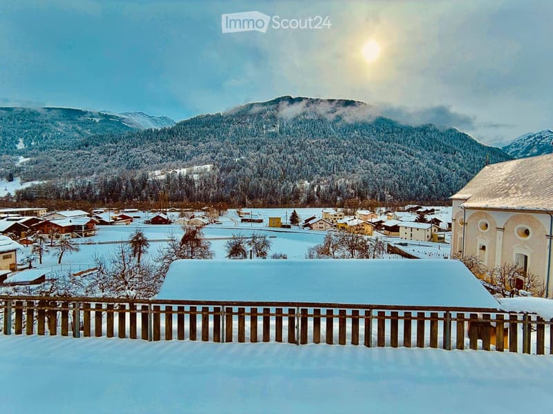 Snowy landscape with a village, mountains, and a church in the background