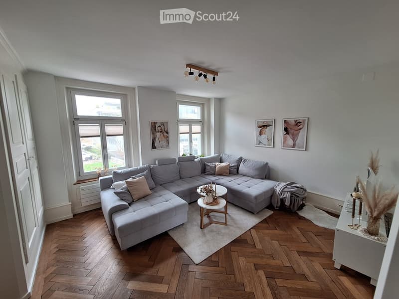 modern living room with gray sectional sofa, wooden coffee tables, white rug, white walls, wooden floor, two windows, and picture frames