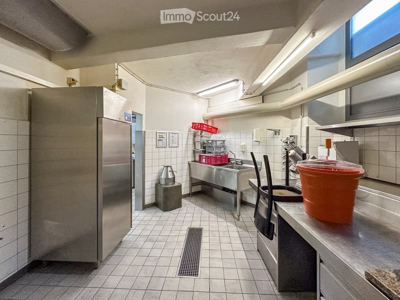Commercial kitchen with stainless steel appliances, tiled floor, sink, refrigerator, and storage boxes