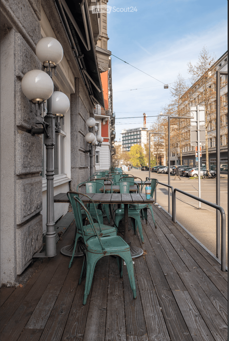 Wooden deck with green chairs and tables, street lamps, and a view of the street