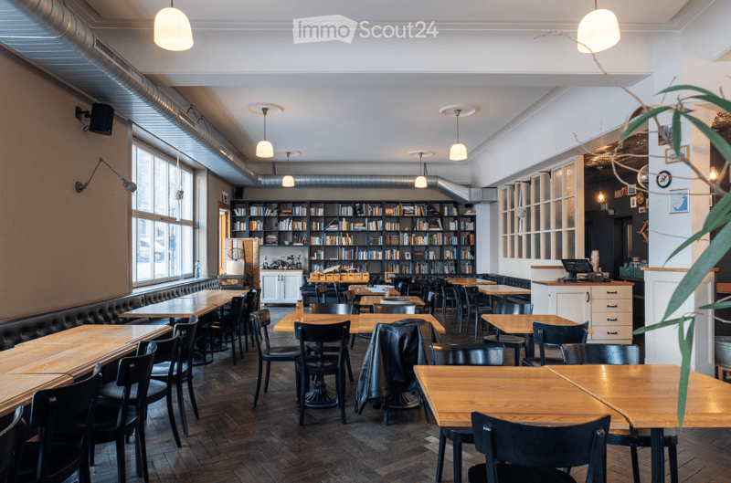 Wooden tables and chairs, bookshelves, lamps, black leather jacket on chair, black speaker on wall, white ceiling, wooden floor