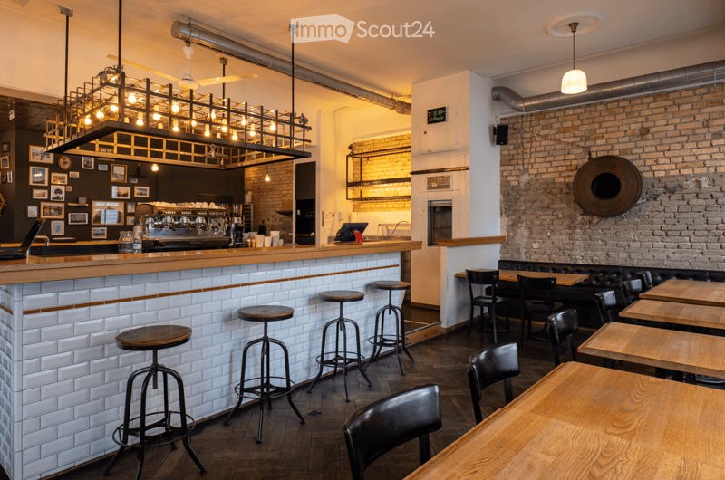 A coffee shop with a counter, stools, tables, chairs, brick wall, and a large chandelier.