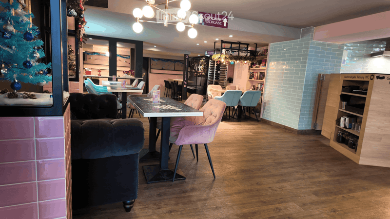Interior of a restaurant with wooden floors, pink and blue tiles, chandelier, decorated table, armchairs, shelves, and Christmas tree.