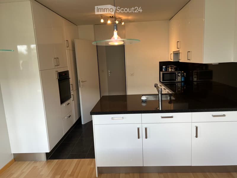 Modern kitchen with white cabinets, black countertops, and stainless steel appliances. Features a central island with a sink and faucet, and a hanging light fixture above.