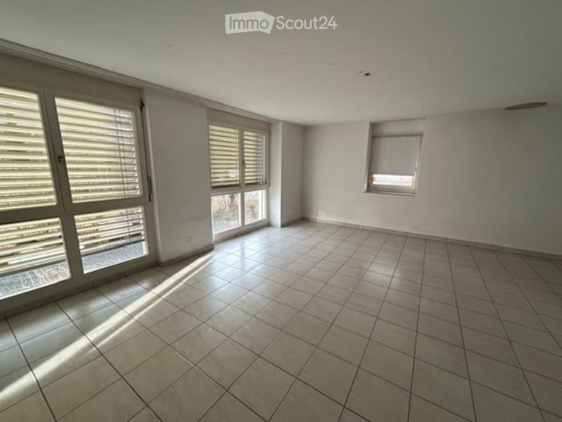 Empty room with white walls, tiled floor, large windows with blinds, and a small window on the right wall.