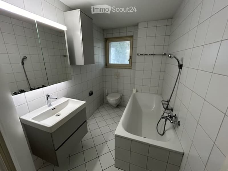 Bathroom with white tiles, bathtub, sink, mirror, toilet, and a window