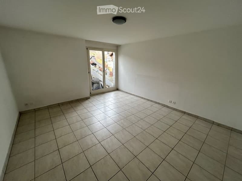 Empty room with white walls, tiled floor, sliding glass door, and a ceiling light.