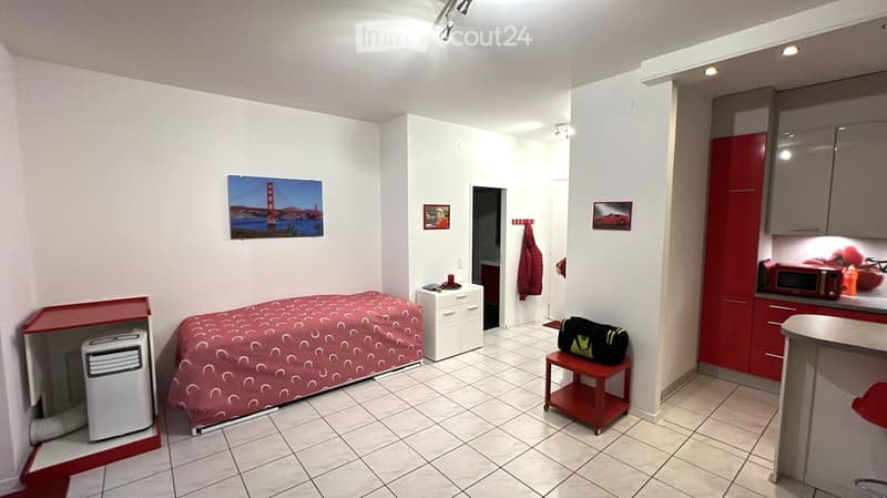 small room with bed, air conditioner, small table, red cabinet, microwave, picture frames, white tiles