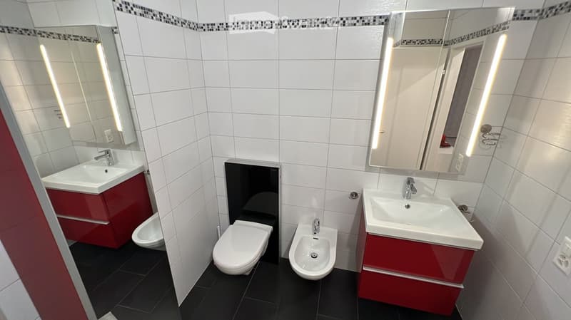 Bathroom with white tiles, red cabinets, two sinks, bidet, toilet, mirrors with lights