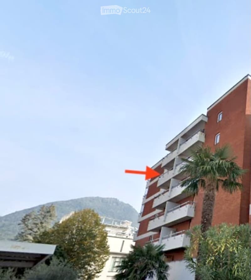 Apartment building, red brick, white balconies, palm trees, mountain in the background