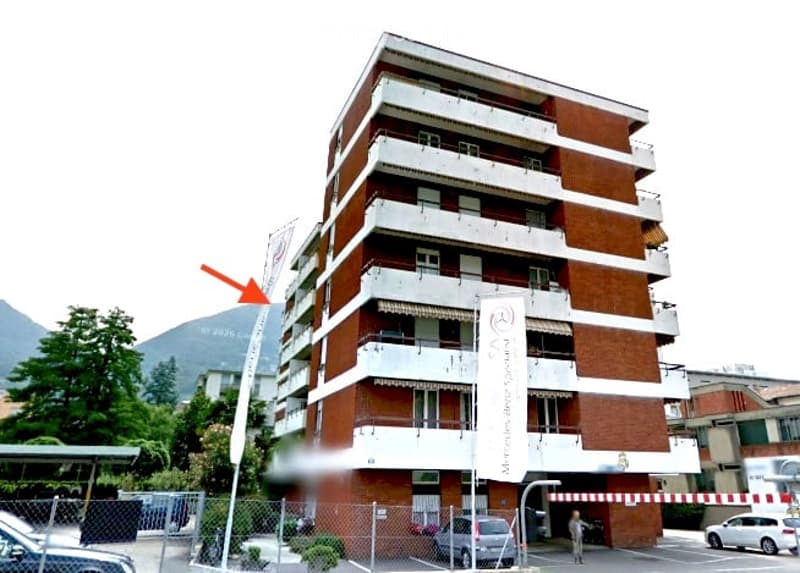 5 story building, brick and white walls, balconies, gated entrance, parking area