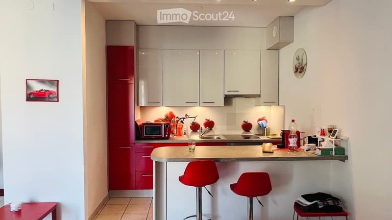 modern kitchen with red cabinets, white countertops, red stools, microwave, sink, refrigerator, and various kitchen items