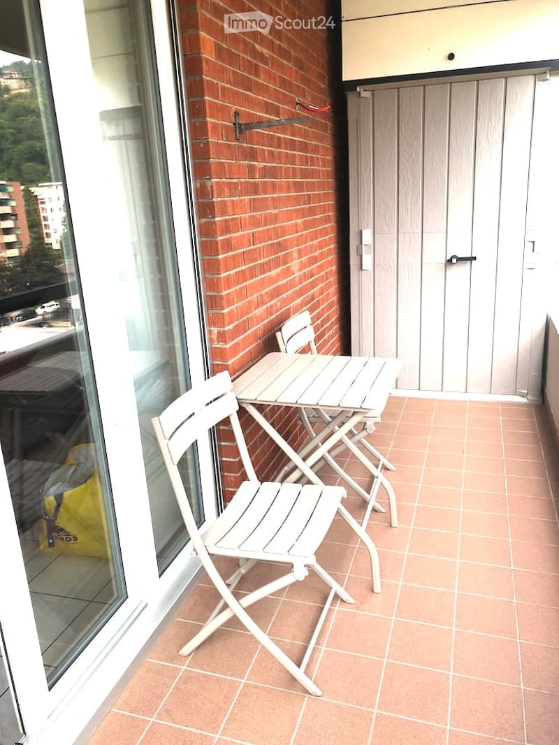 Balcony with table and chairs, brick wall, glass door, yellow bag